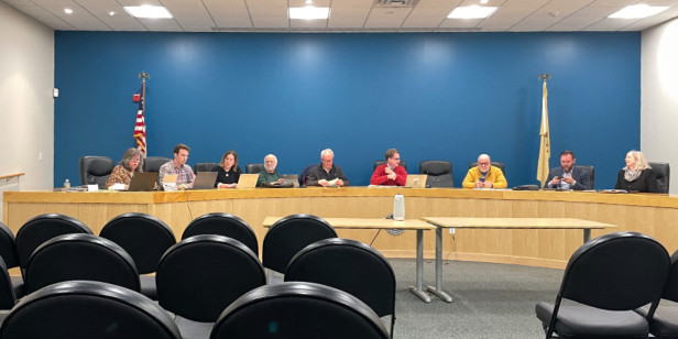 a committee sitting at a desk in front of a room filled with empty chairs