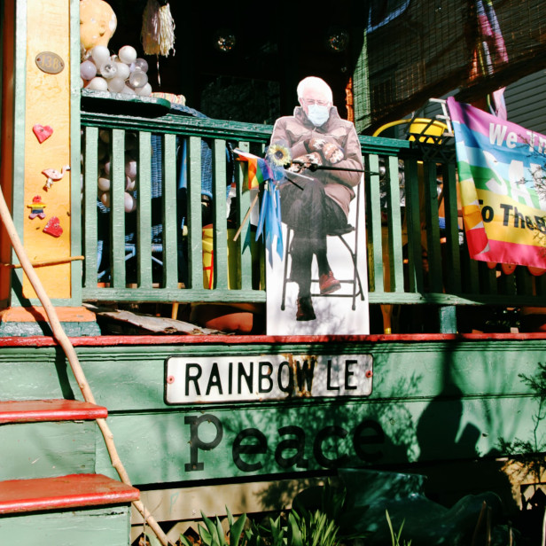 on the front porch of a house is a cardboar cutout of Bernie Sanders sitting on a chair