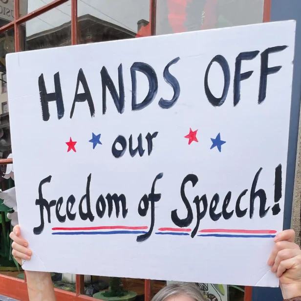 a protest sign that reads hands off our freedom of speech
