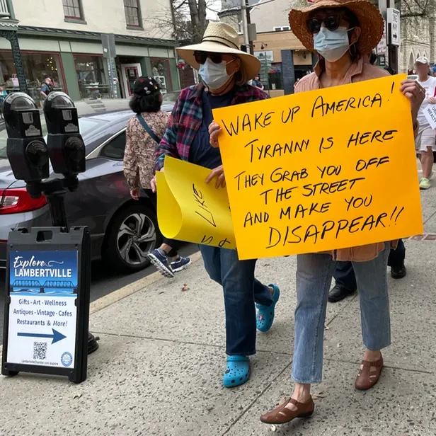 a protester holds a sign that says wake up america, tyranny is here, they grab you off the street and make you disappear