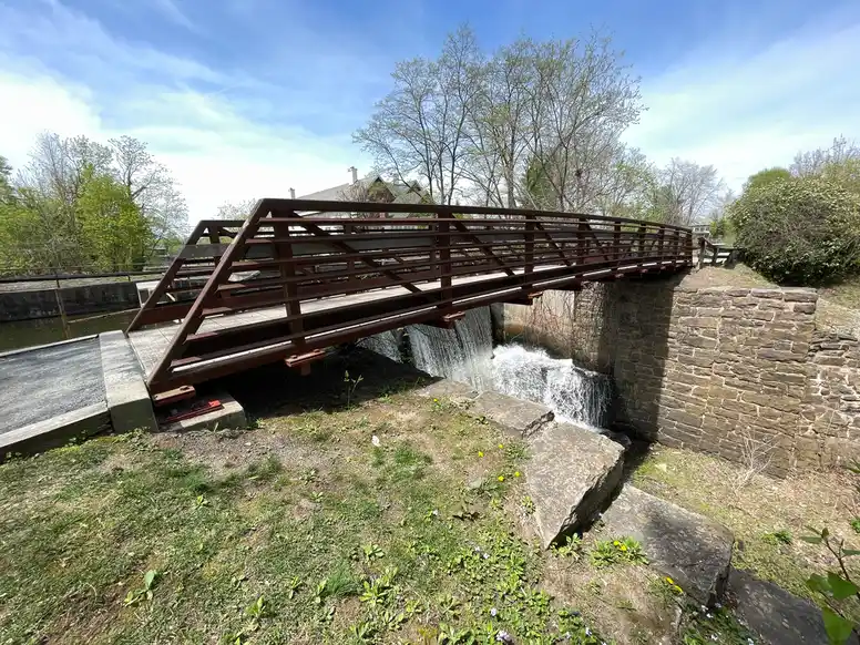 a brown wooden arched bridge crossing a small waterfall
