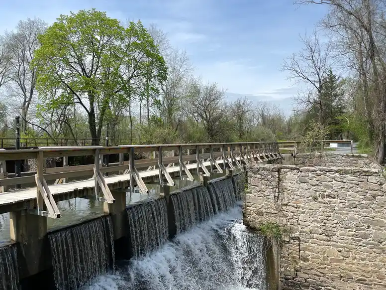 a large waterfall pours under a wooden foot bridge with trees in the distance