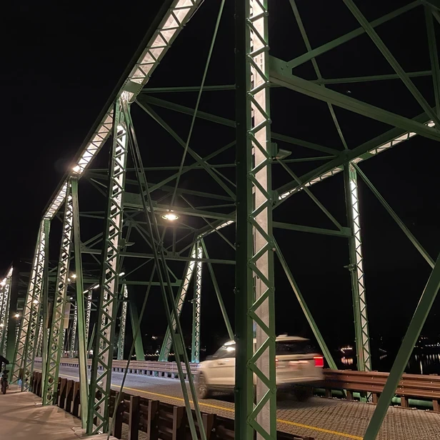 a car drives past the metal support beams on the bridge at night