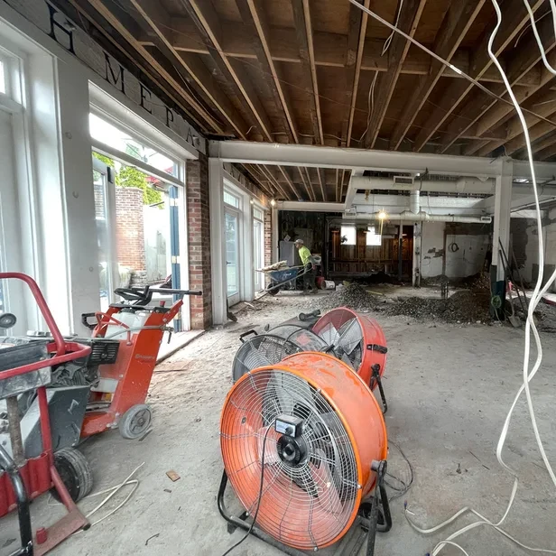 a retail space is under construction with large industrial floor fans, wires, dust, and exposed wood