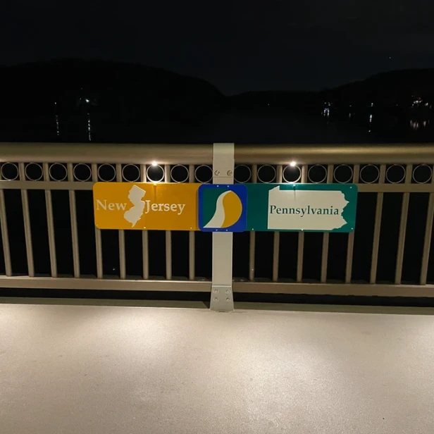 a sign on the bridge railing that reads &ldquo;New Jersey&rdquo; on one side and &ldquo;Pennsylvania&rdquo; on the other
