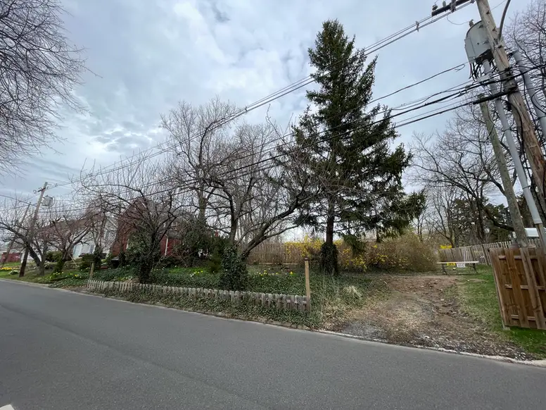 a small red house in the distance next to an empty lot with mature trees