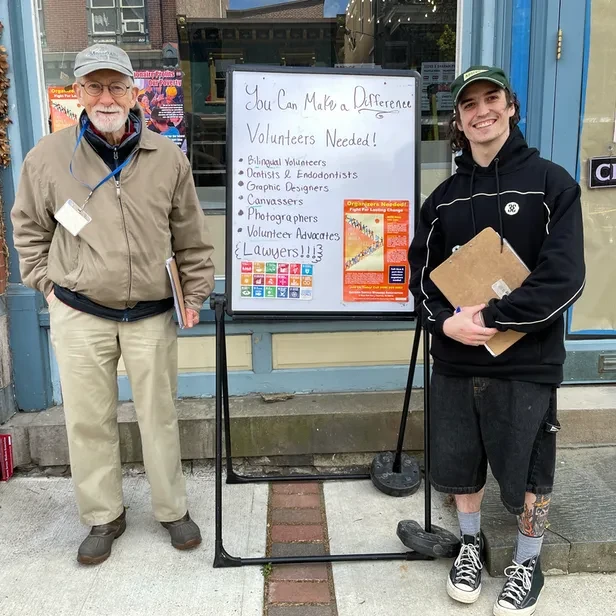 George and Nils standing next to a sign asking for volunteers