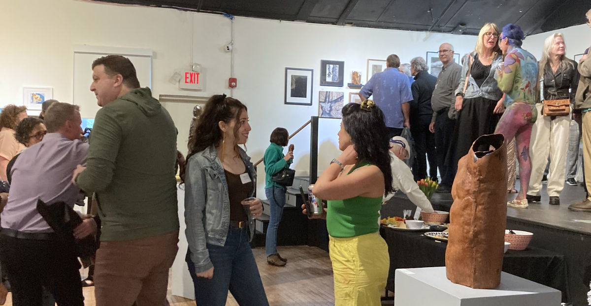 people gathered together, talking and looking at art in a gallery