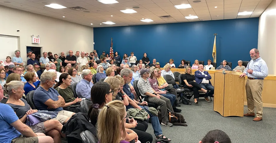 a large group of people sitting and talking with John Connors, who is at the podium