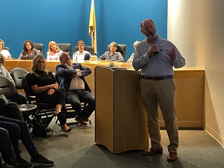 a woman sits next to a man with folded arms and legs, right in front of Connors at the podium