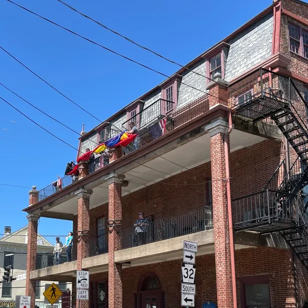 people on a third floor balcony holding a rolled up flag