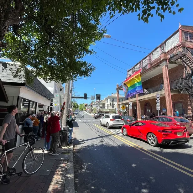 a small group of people watch the unfurling of a large progress pride flag