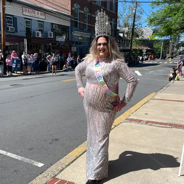 Diva Divine stands by the parade wearing a gown, sash, and crown