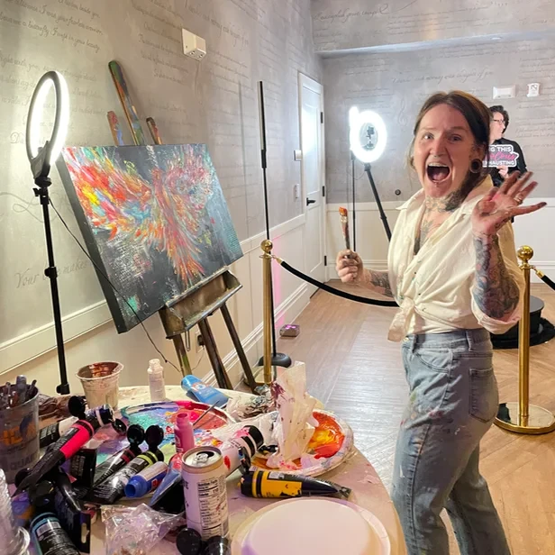 Hope taking a moment to wave at the camera while painting a canvas