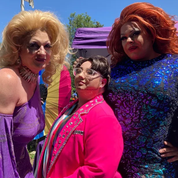 a drag king flanked by two drag queens pose for the camera