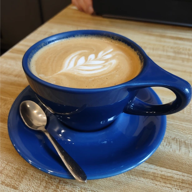  a cup of coffee in a blue mug on a saucer, with a fancy design on the creme of the coffee