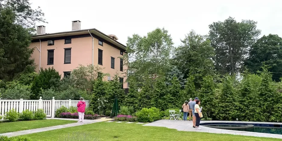 a handful of people wander around the grounds of a garden with manicured grass and a small in-ground pool