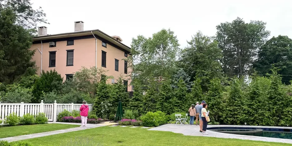 a handful of people wander around the grounds of a garden with manicured grass and a small in-ground pool