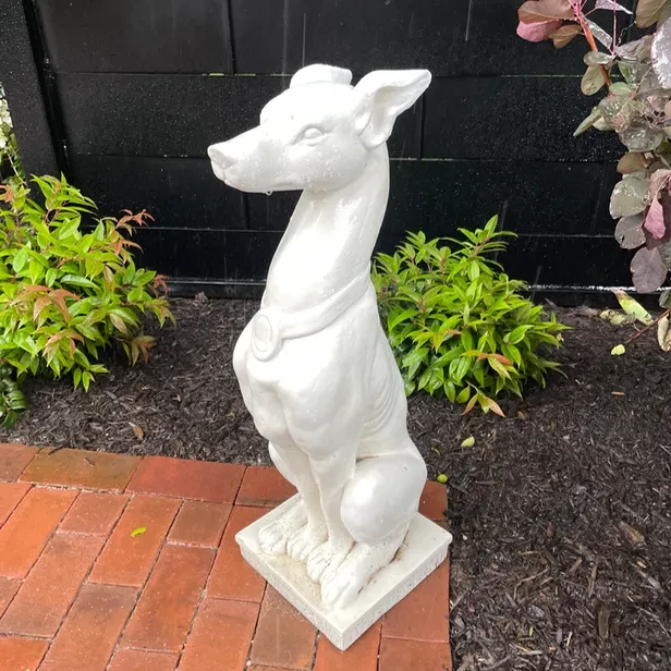 a sculpture of a sitting dog rests on the edge of a brick patio