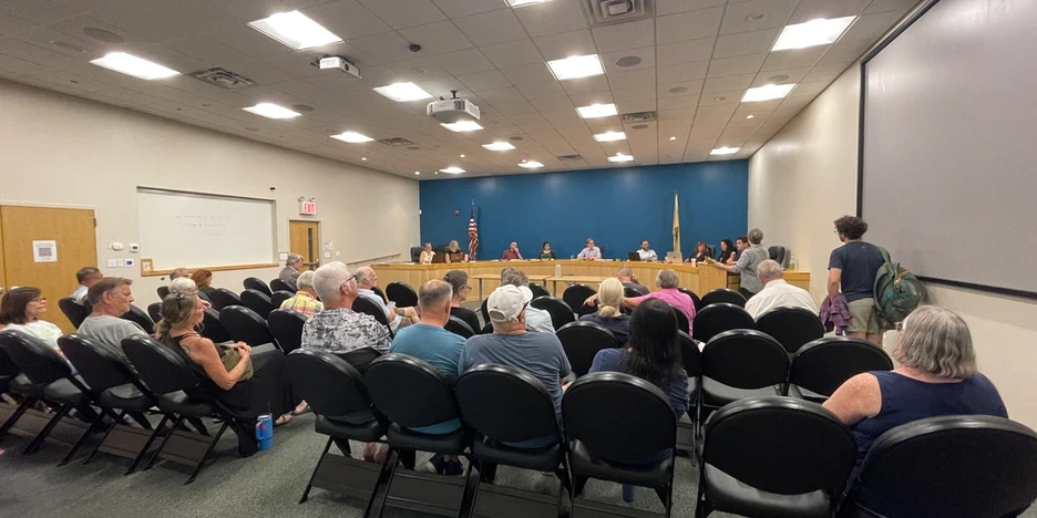 a person speaks to the City Council as citizens sit in chairs before the dais, which is where the Council sits