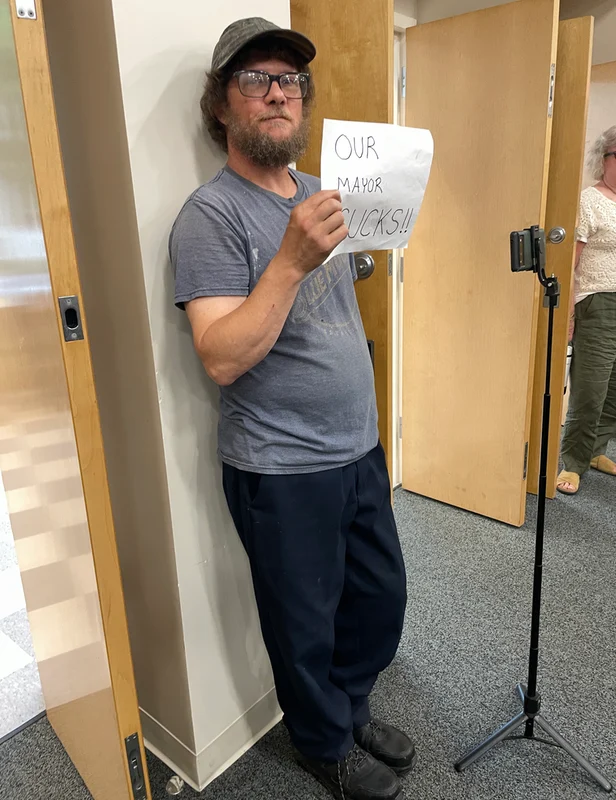 a man holding a sign that reads, “the mayor sucks”