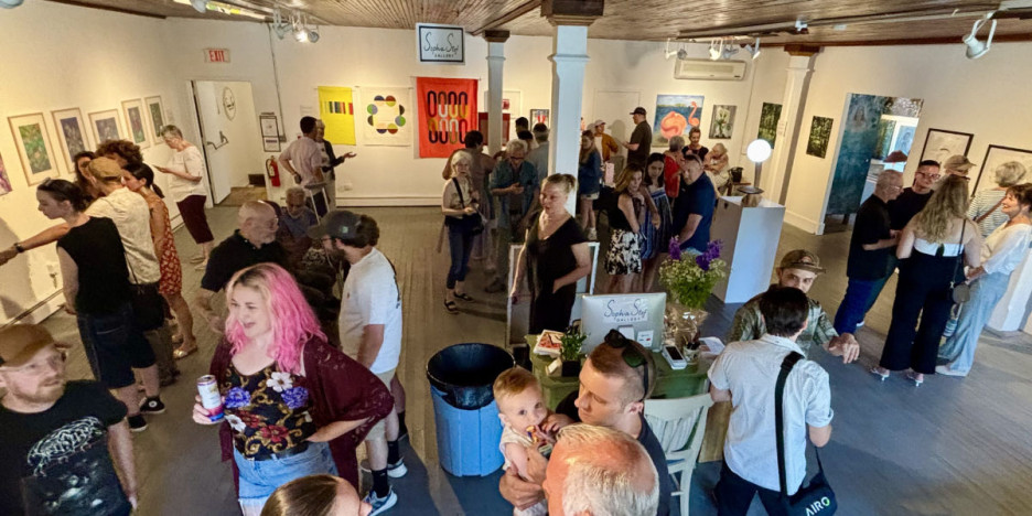 a group of people mingling and looking at art in a gallery space