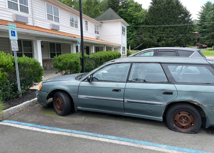 an old Subaru wagon with a flat tire is parked in the accessible parking spot