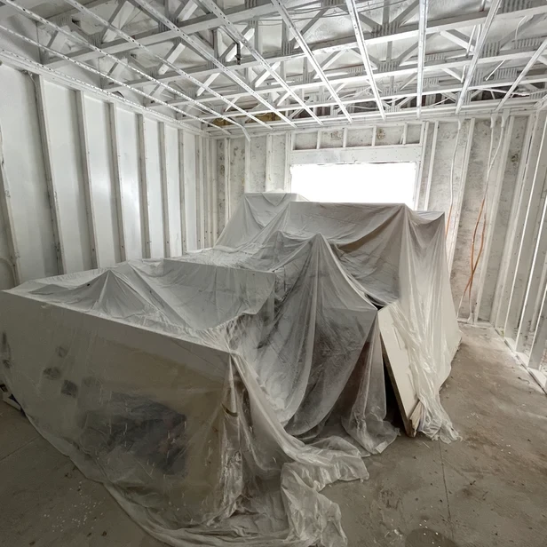 a pile of fixtures covered in dropcloths in the middle of an empty, gutted apartment