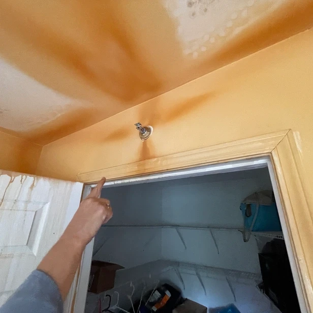 Linda points at the sprinkler spigot, which is surrounded by rust stains on the wall around it