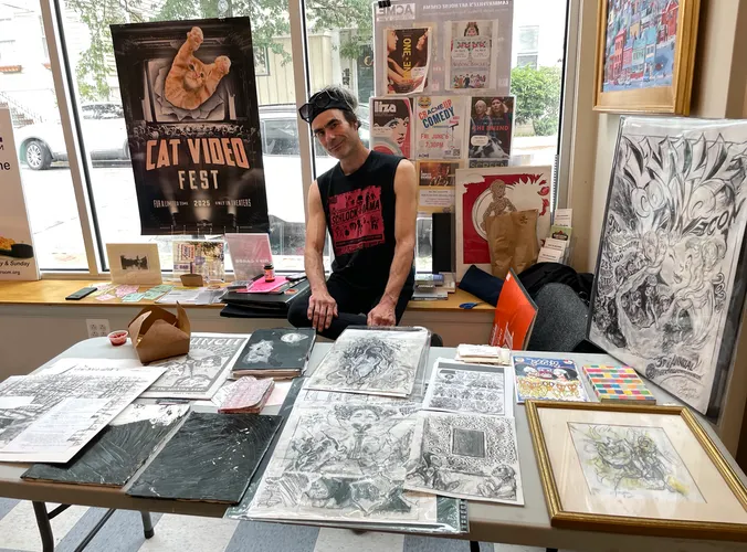 Jacques sitting behind his table, which has original artworks displayed on it
