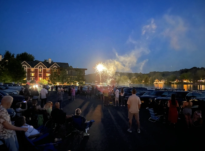 people in a parking lot enjoy fireworks exploding over the Delaware river