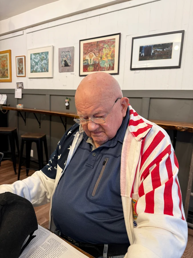 a man wearing an American flag jacket reading a book inside Union Coffee