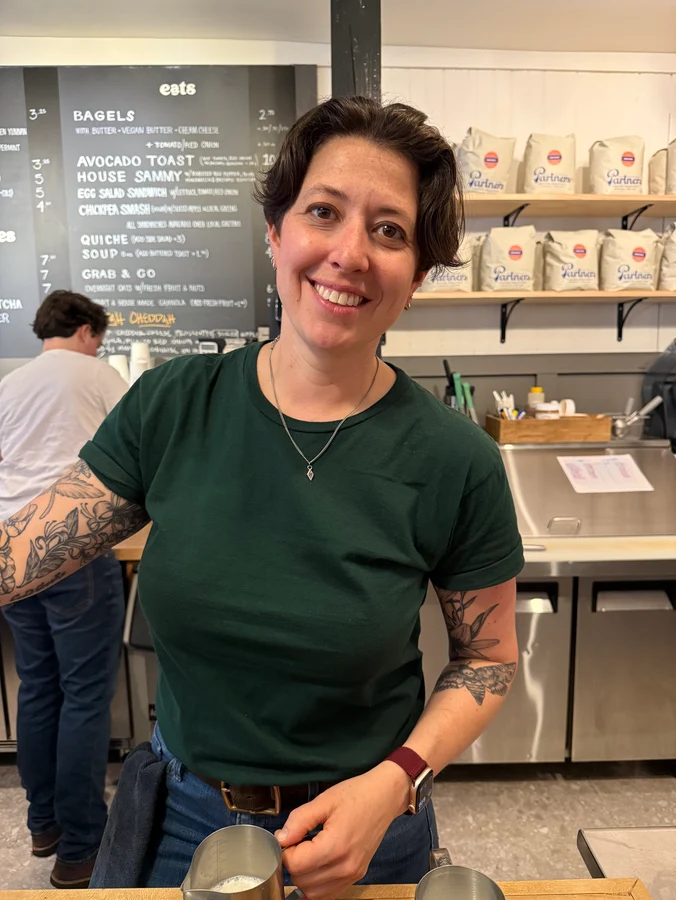 a smiling woman pauses for a photo while making coffee