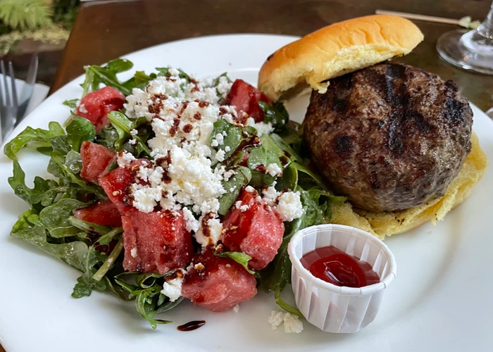 a fat burger with a side salad, and ketchup on the side, on a white plate