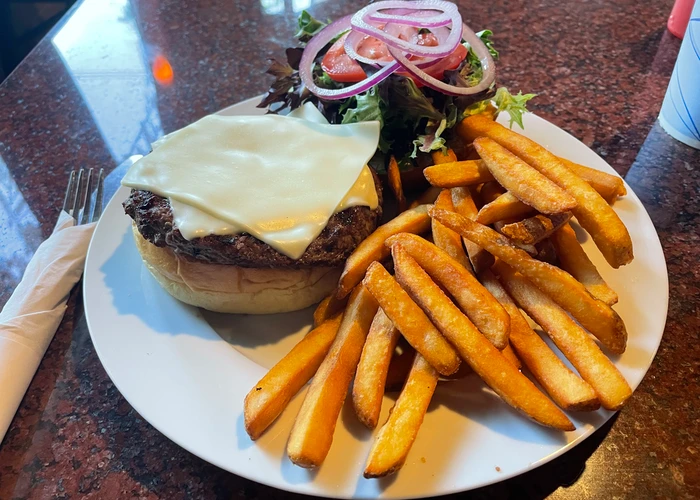 a cheeseburger on a bun with onions, tomato, lettuce, and a side of crispy fries on a white plate