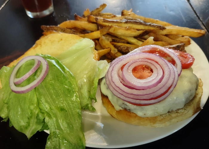 a burger on a bun with bacon, cheese, lettuce, tomato, onion, and a side of potato wedges