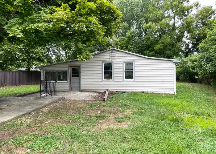 a small, old house on a grassy lot with a tree in the front yard