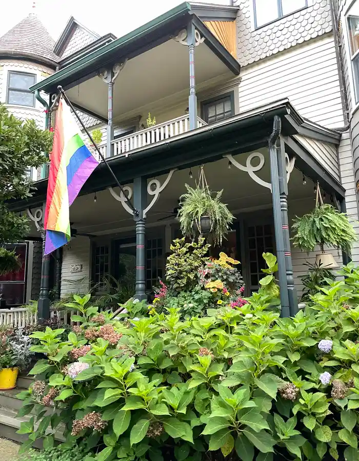 a rainbow flag hangs outside the front door next to a large bush