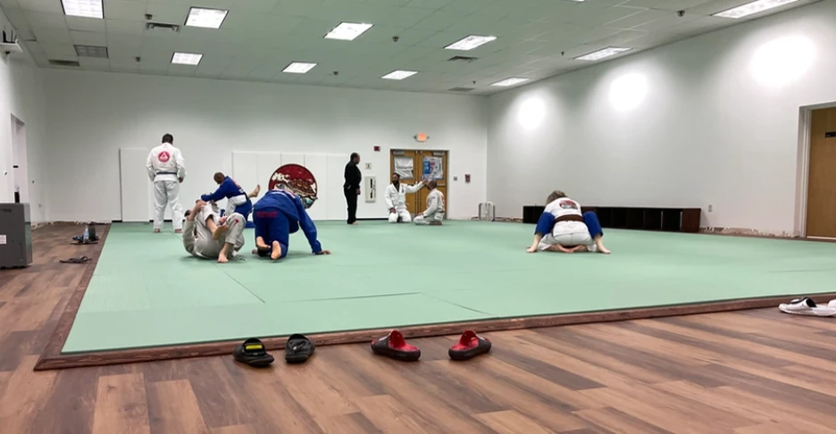 a group of students practice jiu-jitstu on a mat inside the dojo