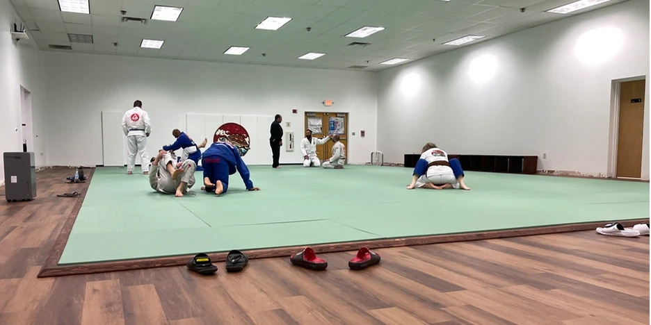 a group of students practice jiu-jitstu on a mat inside the dojo
