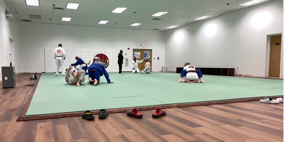 a group of students practice jiu-jitstu on a mat inside the dojo