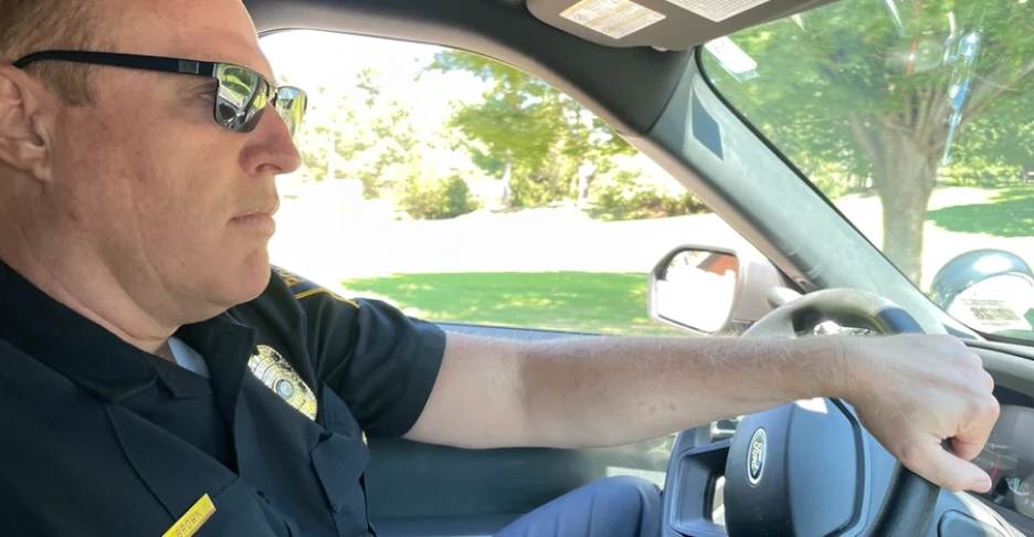 Robert Brown, a police officer, wearing sunglasses, drives a police cruiser with his hand on the steering wheel
