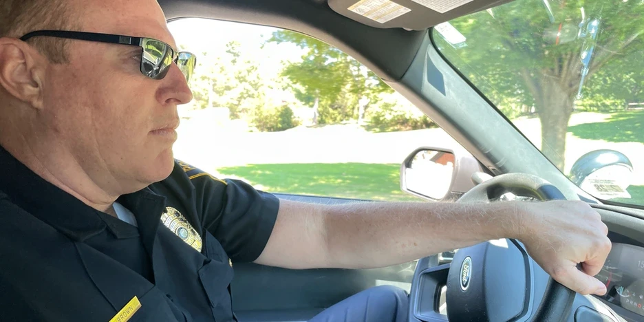 Robert Brown, a police officer, wearing sunglasses, drives a police cruiser with his hand on the steering wheel